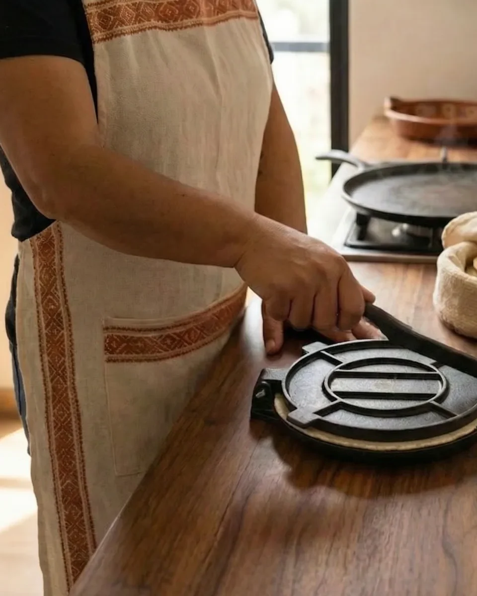 Mujer con mandil bordado prensando una tortilla con la prensa METZAL